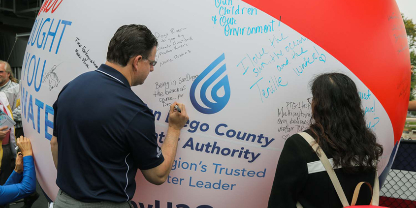 Attendees sign the "Brought To You By Water" symbolic beach ball, naming summer activities that rely on a safe and reliable water supply. Photo: Water Authority. Brought To You