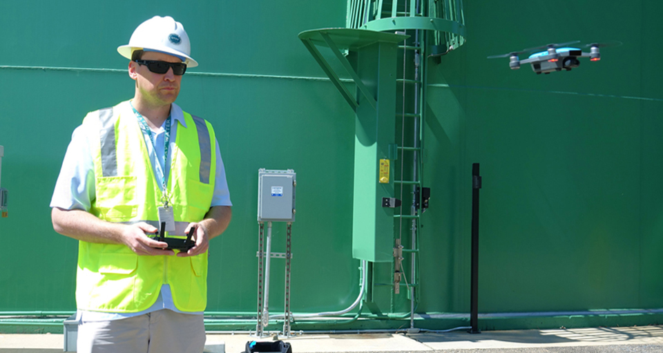 Alexander Schultz, Otay Water District geographic information systems technician, operates a drone in front of a district water storage tank. Photo: Otay Water District 65 Years