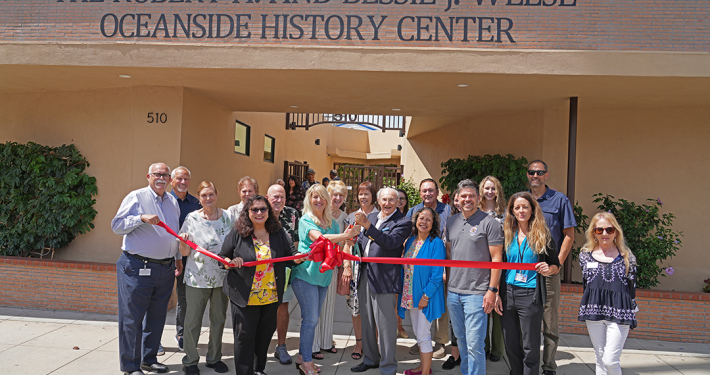 Tom Weese, son of Robert and Bessie Weese and historian Kristie Hawthorne perform the ribbon cutting at the new location of the Weese Oceanside History Center with members of the Oceanside Historical Society. Photo: Zach Cordner/The Osider.