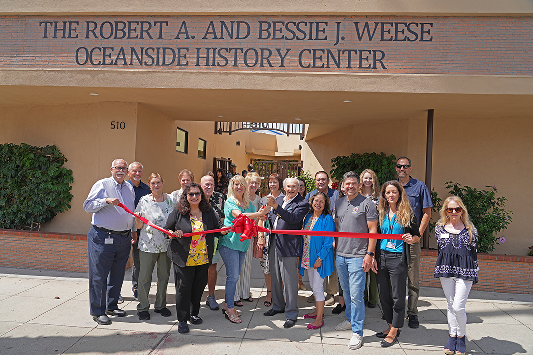 Tom Weese, son of Robert and Bessie Weese and historian Kristie Hawthorne perform the ribbon cutting at the new location of the Weese Oceanside History Center with members of the Oceanside Historical Society. Photo: Zach Cordner/The Osider.